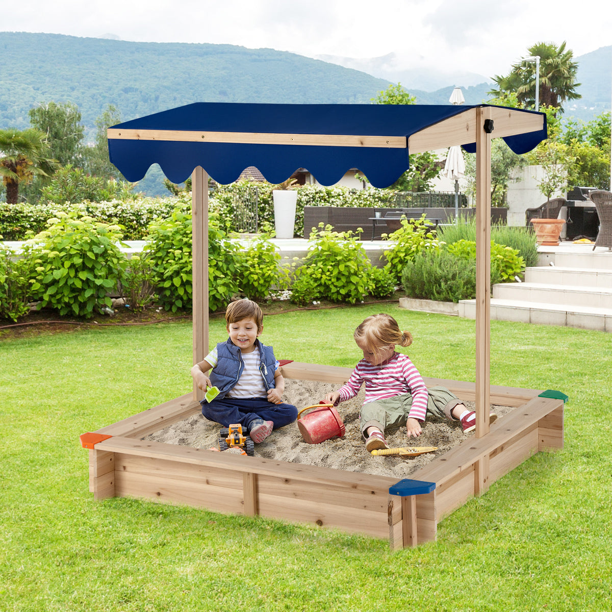Children playing in the wooden sandbox in a garden with green bushes and a patio