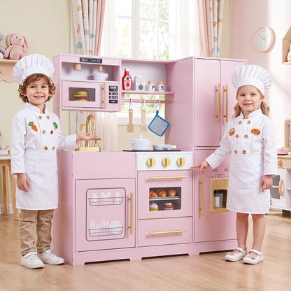 Two children in chef hats and aprons stand by the pink play kitchen