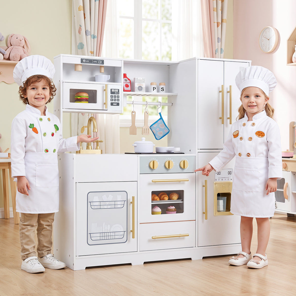 Two children in chef outfits smile and play with the white wooden play kitchen