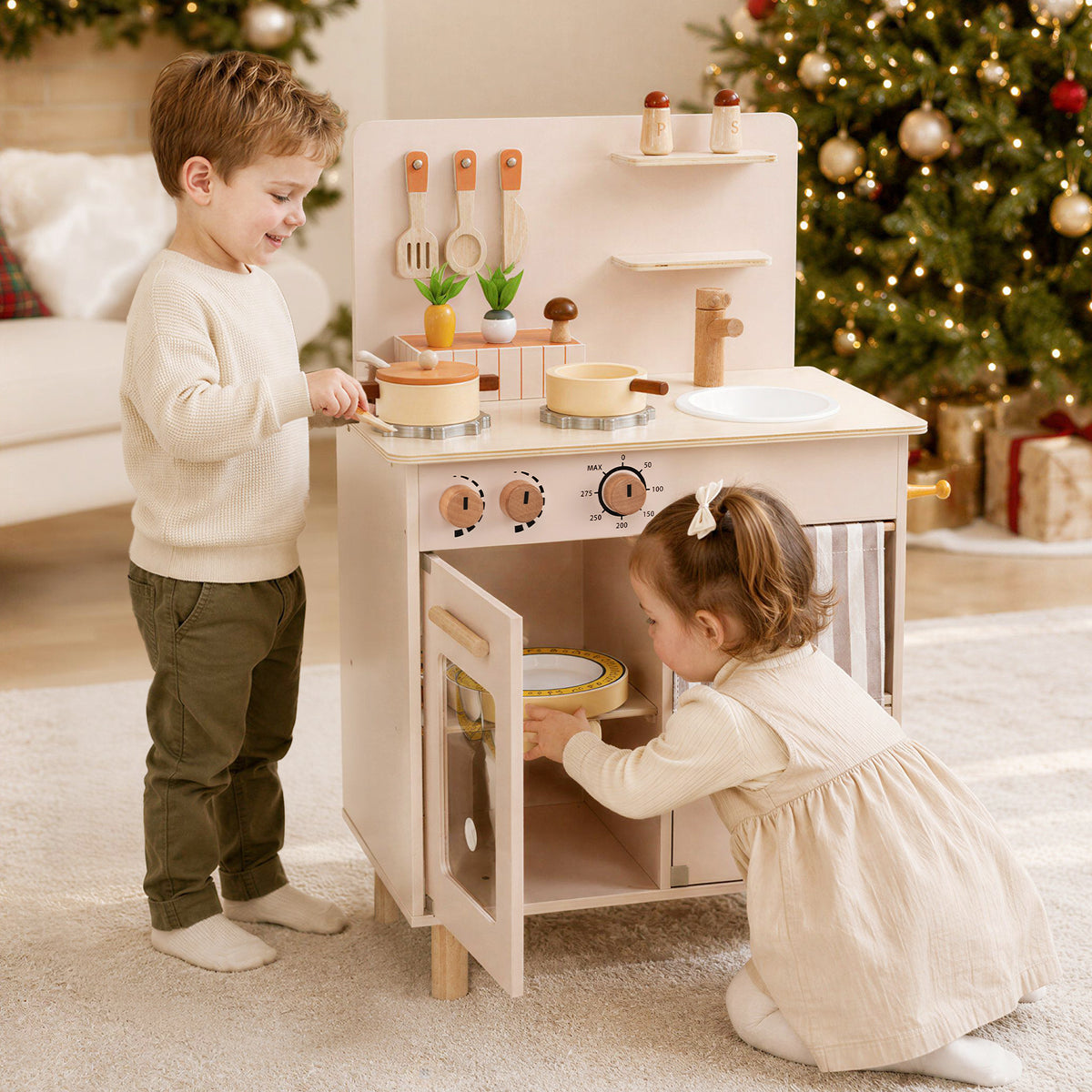 Two children playing with the play kitchen set in front of a Christmas tree