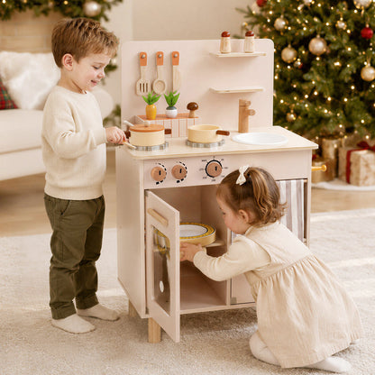 Two children playing with the play kitchen set in front of a Christmas tree
