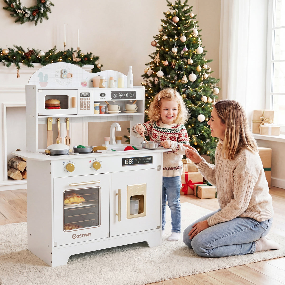 A mother and daughter interact with the white play kitchen set in a festive living room