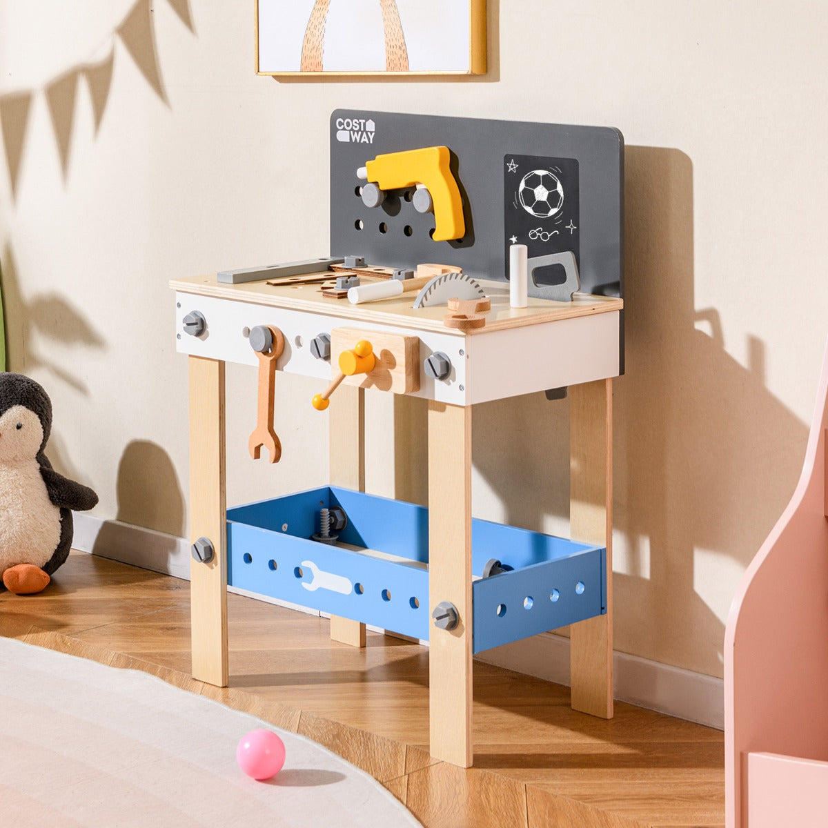The wooden toddler workbench playset set up in a child's bedroom with toys around