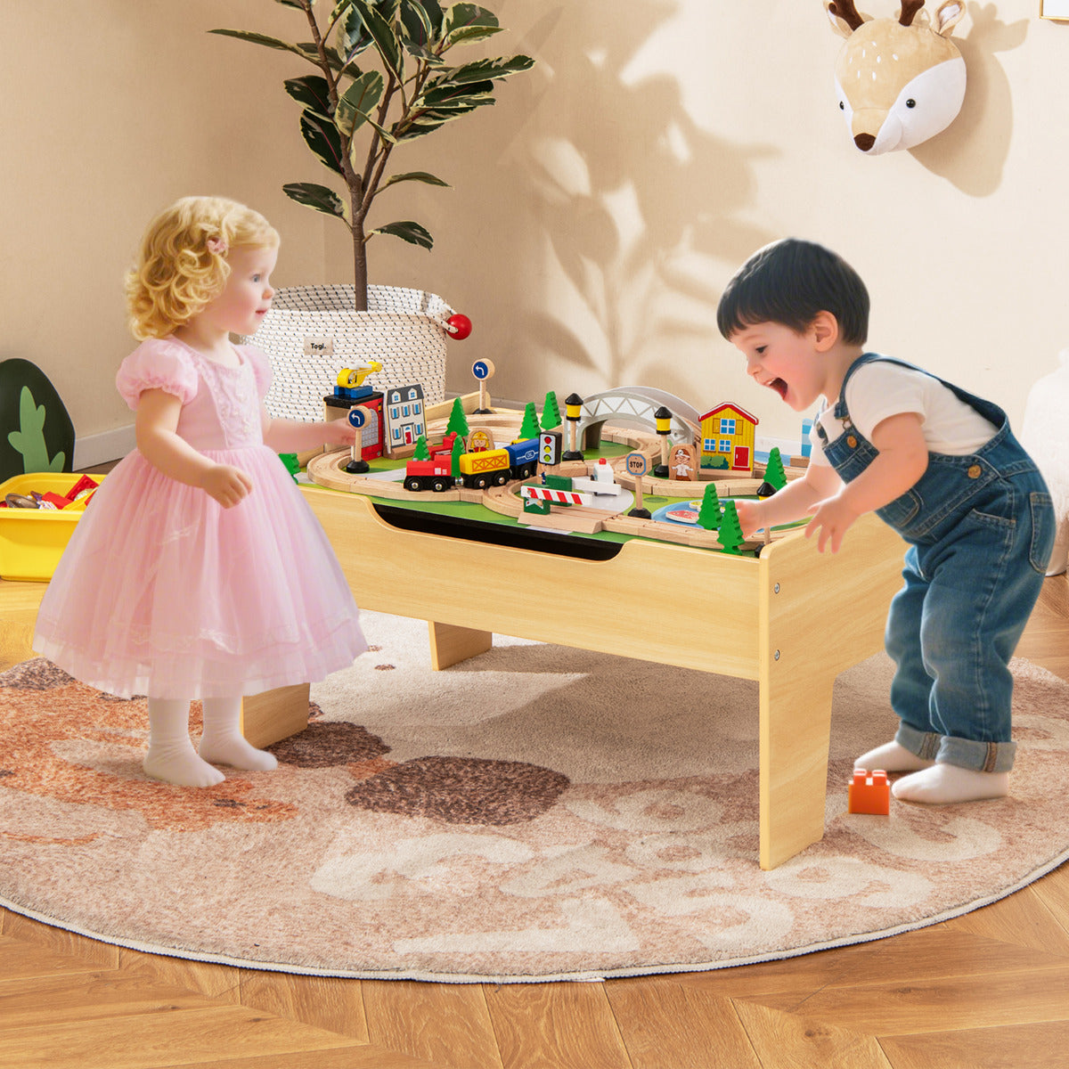 Two young children playing with the wooden train table activity set in a living room