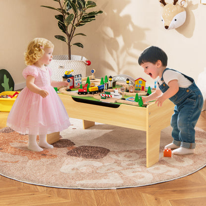 Two young children playing with the wooden train table activity set in a living room